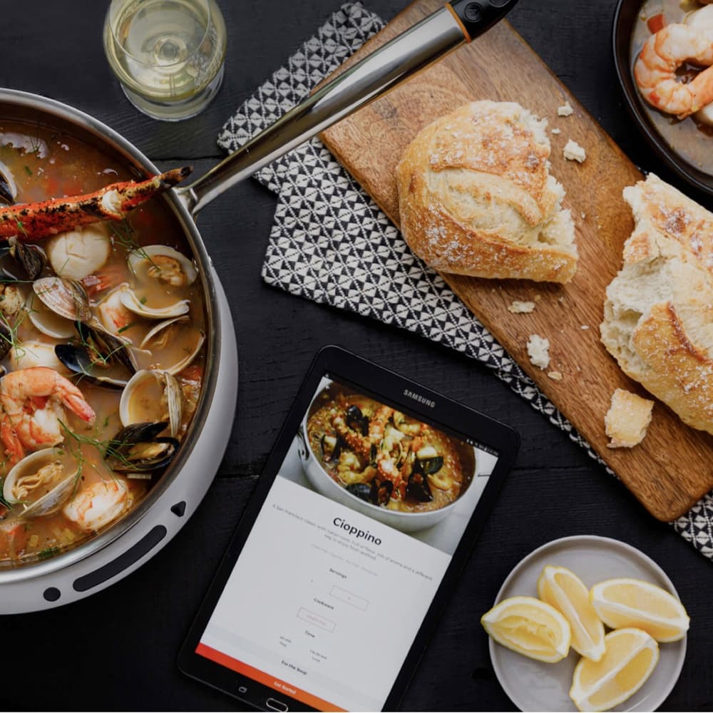 Hestan Cue pan of cioppino beside a tablet showing the guided recipe